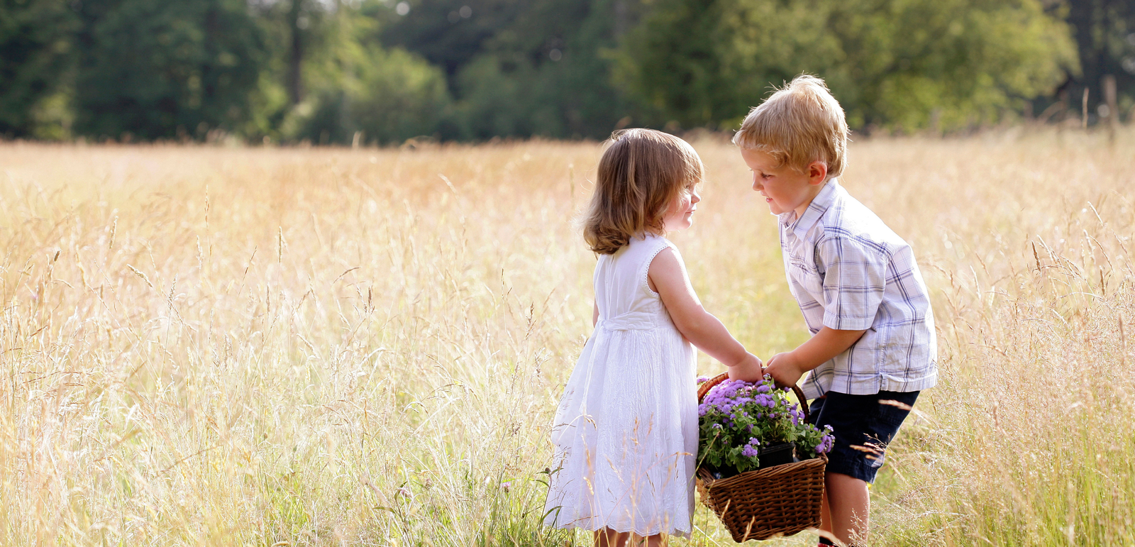 little boy helping little girl carry basket of flowers in a field